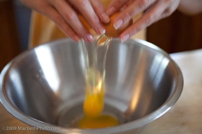 Preparing eggs by cracking each into steel bowl.