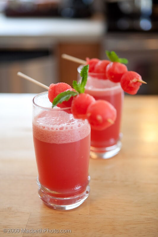 Watermelon Juice Coolers with melon balls and mint on a bamboo skewer as garnish.