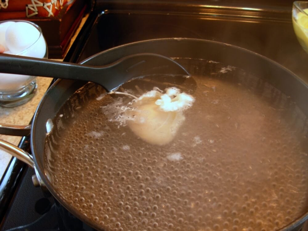 Scooping poached egg with a slotted spoon.