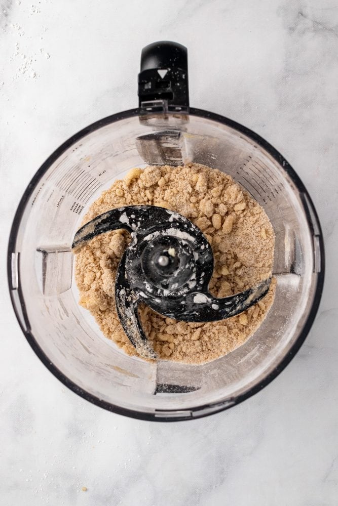 Overhead view inside a food processor of the topping mixture with a crumble texture the size of peas.