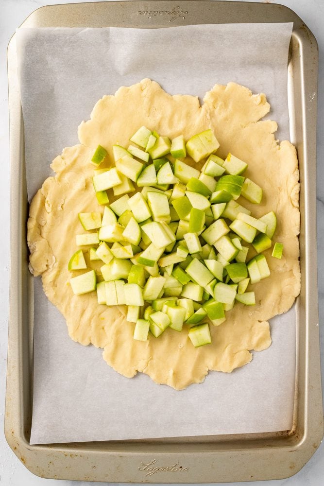 Overhead view of diced apples ontop of dough rolled out onto a lined sheet pan to form into apple crostata.
