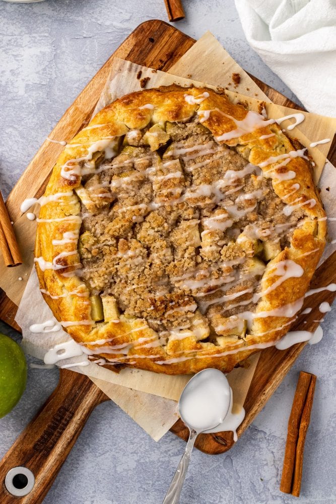 Overhead view of baked apple crostata on a wood board, a spoon with sugar drizzle off to the side.
