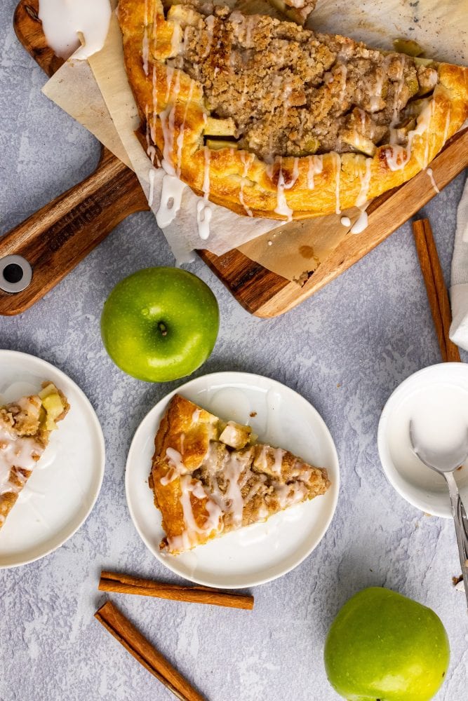 Overhead view of serving a slice of apple crostata, a single slice on a plate and green apples to the side for decoration.