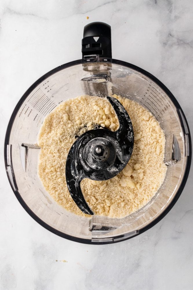 Overhead view of butter and dry ingredients pulsed together in food processor, the texture a bit crumbly.