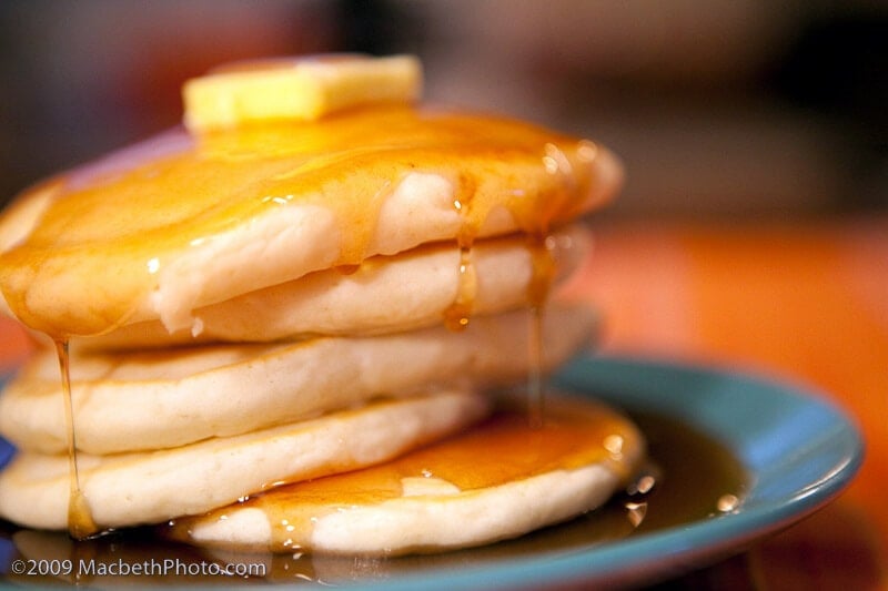 A photo of five pancakes stacked on a blue plate, covered in syrup with a dab of butter on top. There is a copyright watermark in the corner for 2009 Macbeth Photo.