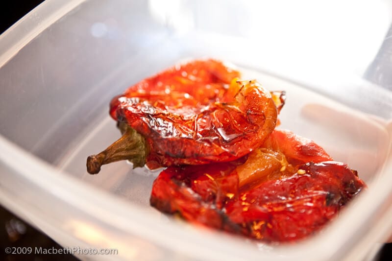 Resting the roasted red peppers in a container to let them cool.