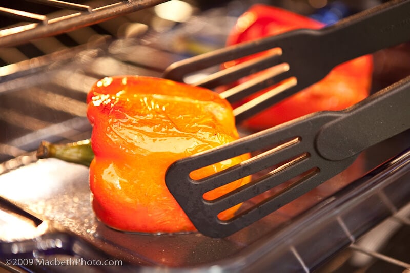 Turning the red peppers over with tongs.