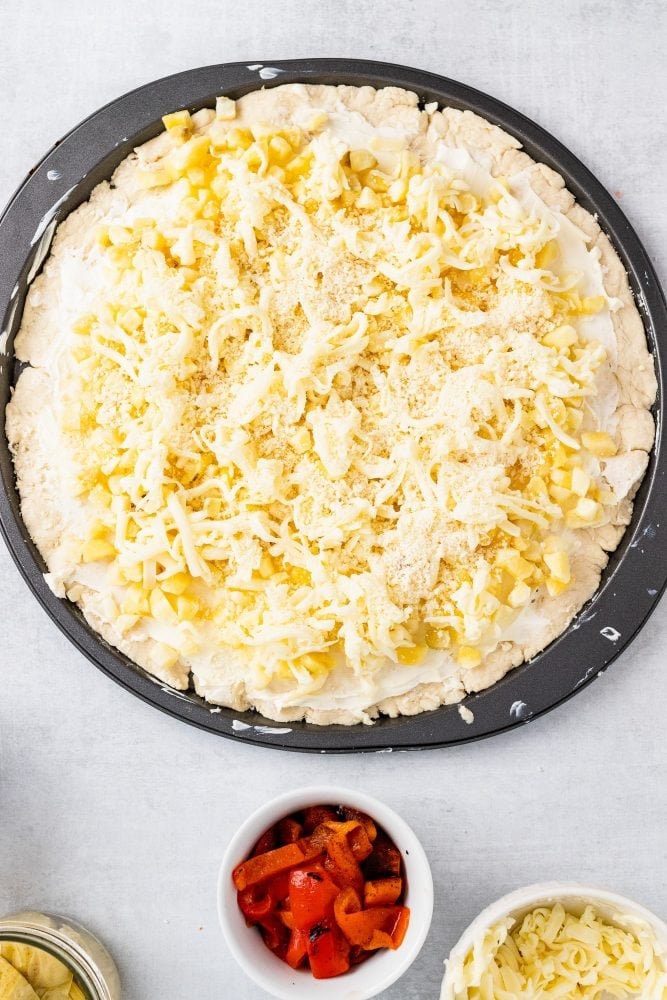 Overhead shot of sprinkling the hash browns and cheeses on top of the round biscuit dough in a pan.