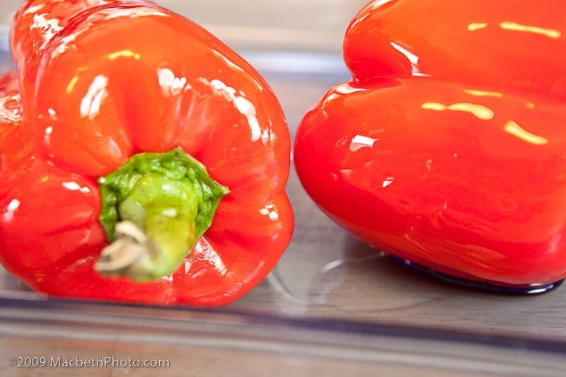 Red peppers coated in olive oil and placed in a baking pan. TheTravelBite.com