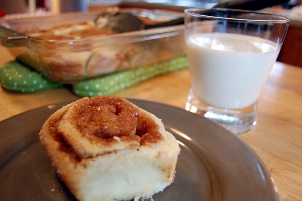 Homemade cinnamon roll on a plate with a glass of milk on the side.