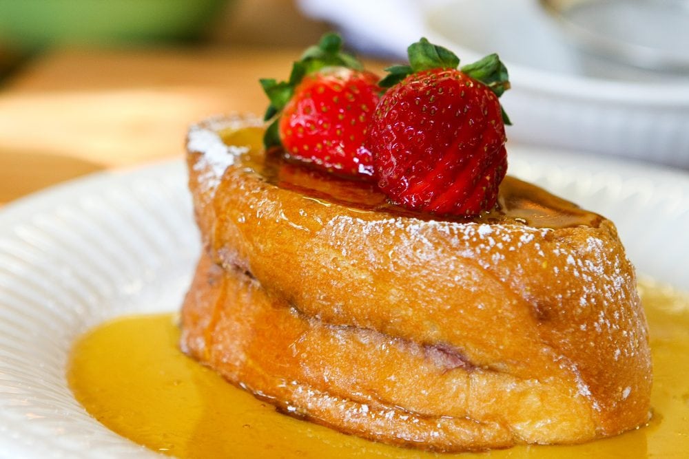 Ricotta & Raspberry Stuffed French Toast with sliced strawberries and maple syrup.