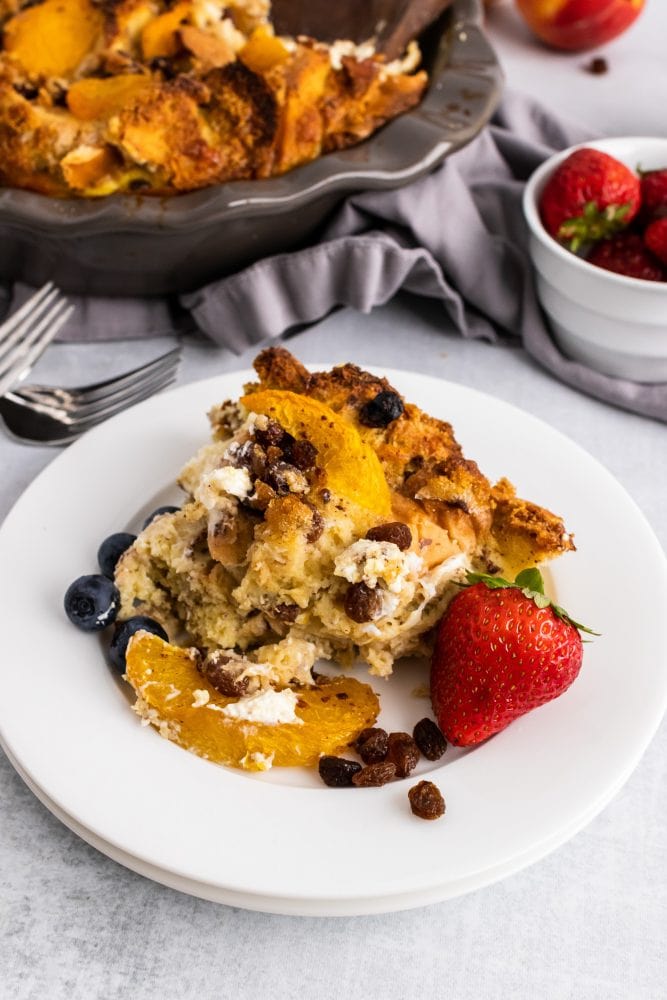 Slice of bread pudding on a plate with peach, strawberry, and blueberries.