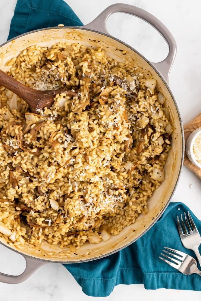 A large pot of cooked Champagne risotto with mushrooms and cheese being scooped out with a wooden spoon.