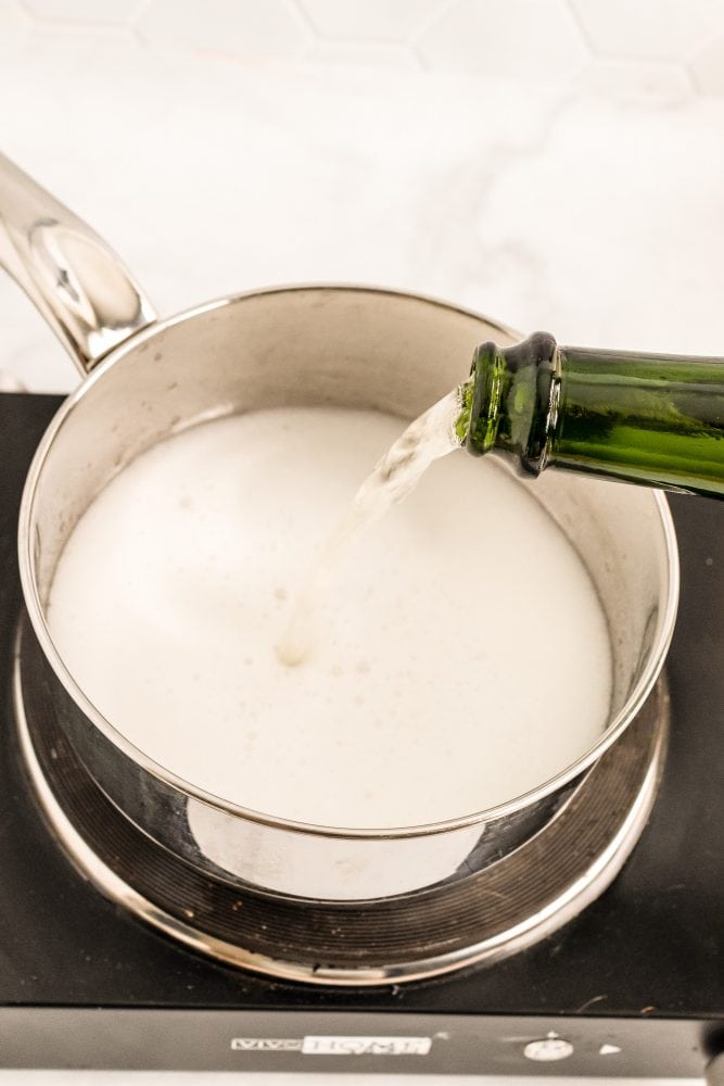 Carefully pouring Champagne into sauce pot.