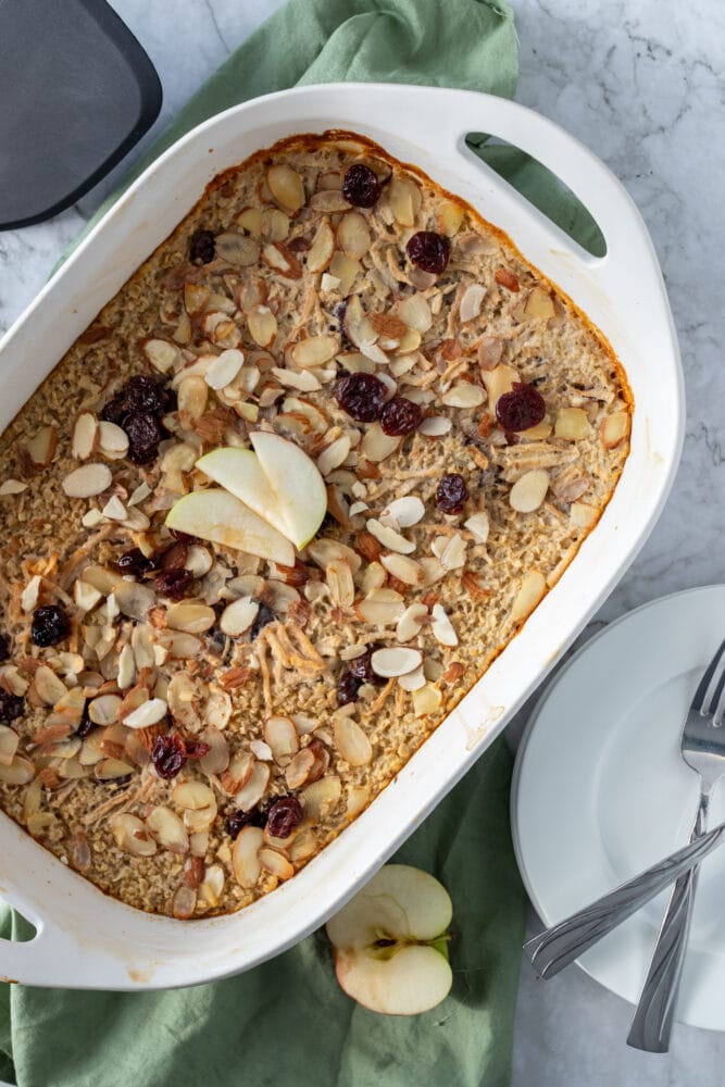 Overhead shot of cherry almond oatmeal bake with sage green towel, sliced apple, dried cherries, and toasted almonds.