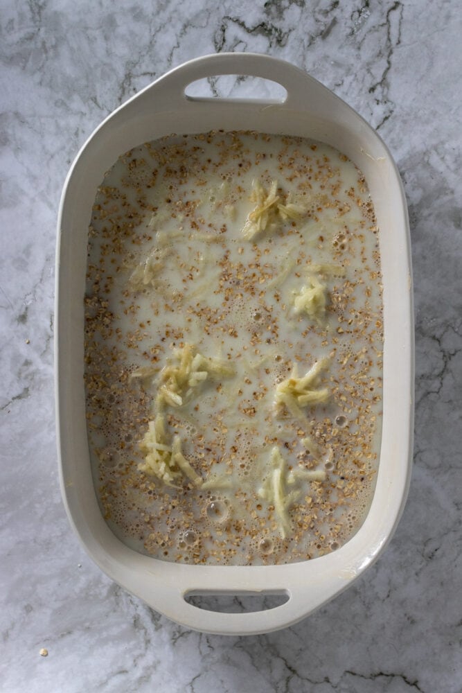 Overhead shot of milk, oatmeal, and grated apple in baking dish.