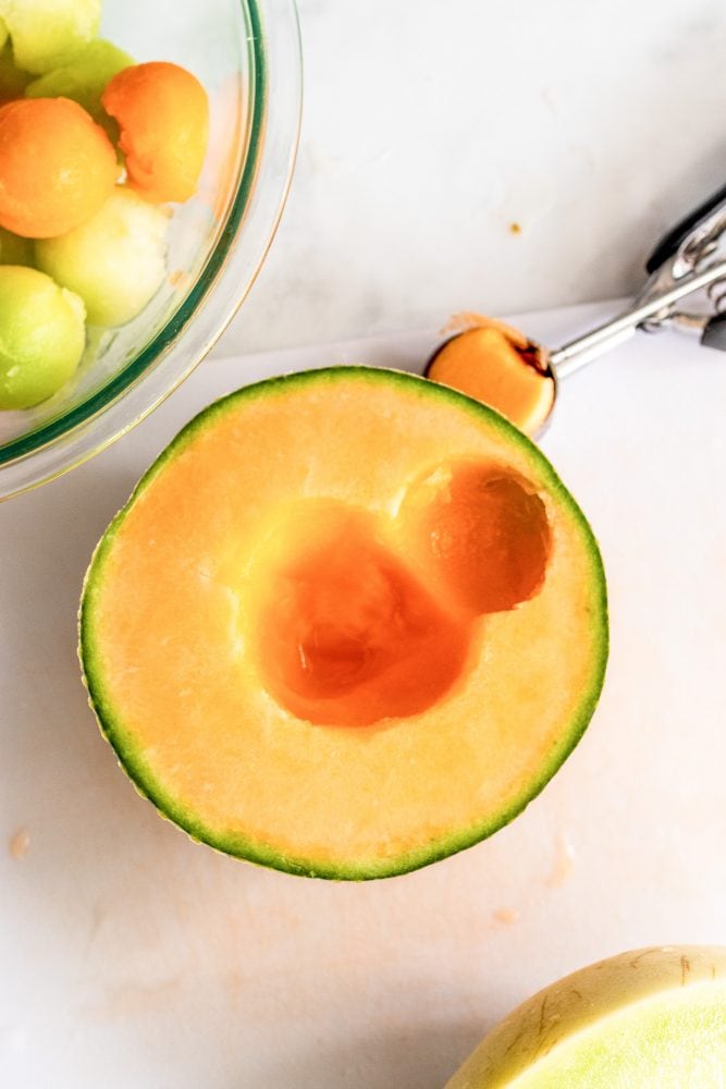 A melon baller taking a round scoop out of the cantaloupe. 