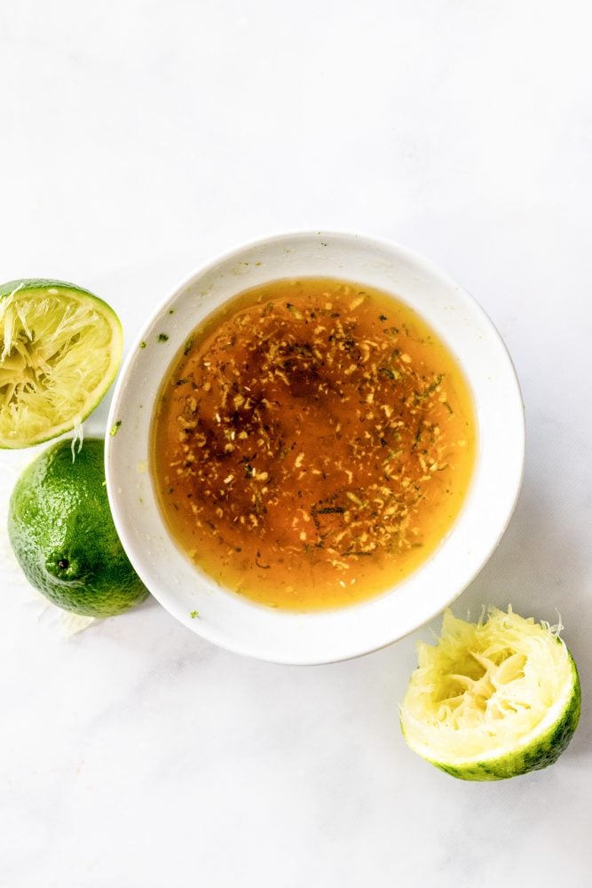 A bowl of the honey ginger lime marinade with fresh squeezed limes on the side.