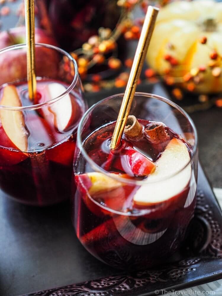 Glass of Fall Sangria with red wine, apple slices, and cinnamon sticks served with a gold straw.