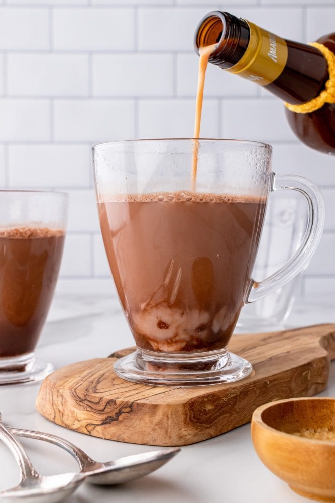 Pouring amarula into a clear mug of hot chocolate.