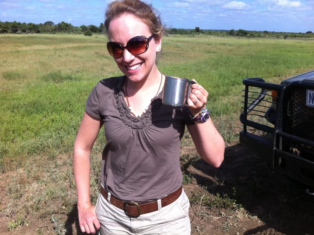 Rachelle on safari in South Africa, standing in a field next to a jeep holding a mug.