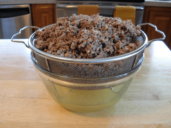 Cooked ground beef and pork in a strainer over a bowl that is catching the drained broth.