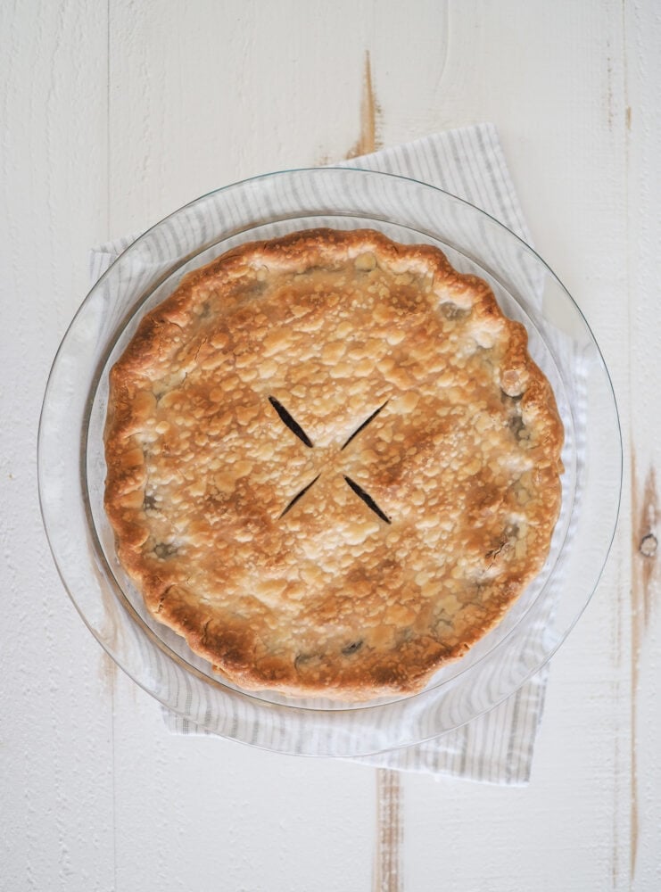 Overhead photo of a whole tourtiere (meat pie) unsliced and cooling on a white and grey striped towel.
