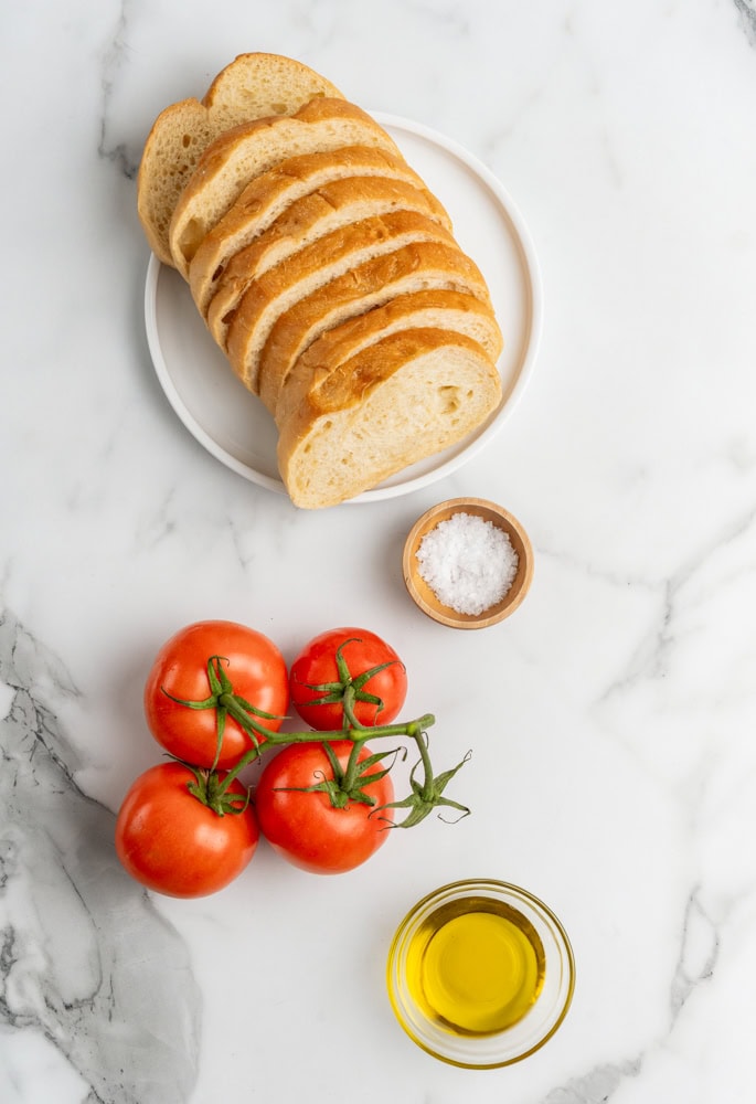 Ingredients to make pa lamb tomaquet including rustic bread, sea salt, tomatoes, and olive oil.