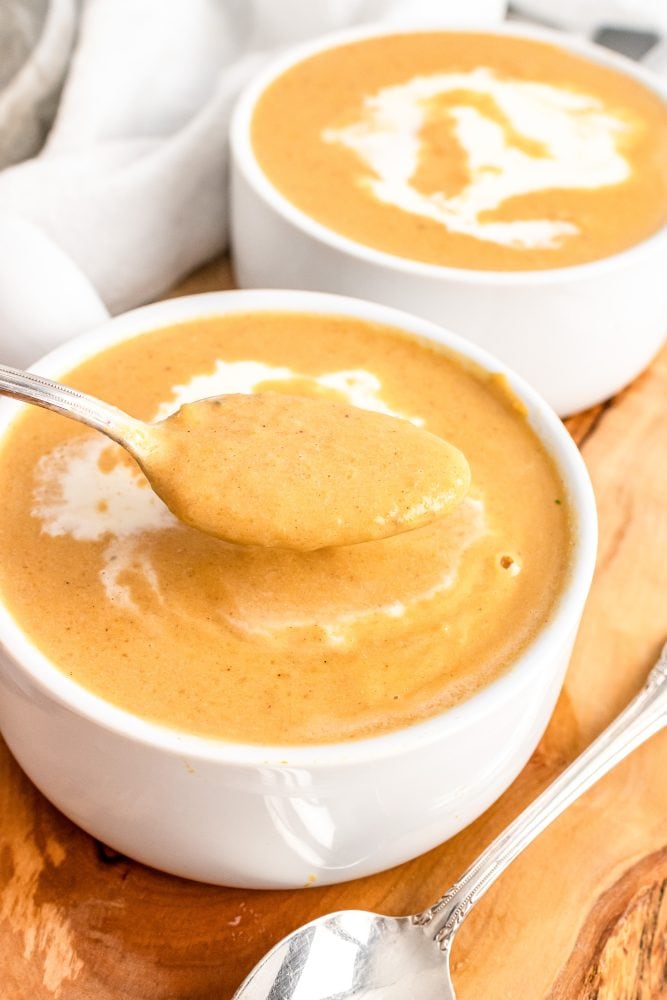 Two soup bowls filled with butternut squash soup and a spoon lifting a bite out of one.
