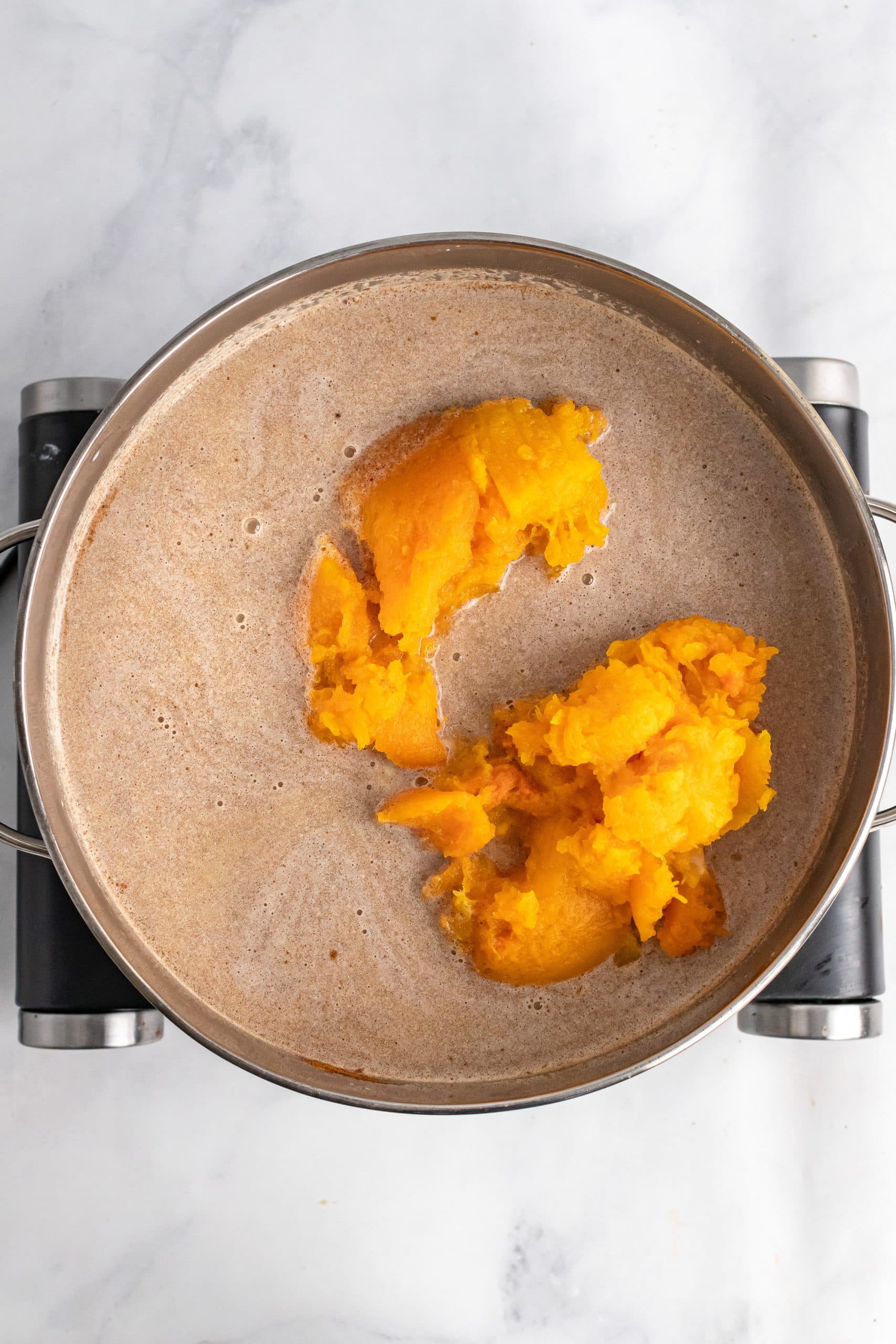 Adding roasted butternut squash to pot full of spices simmered with milk.