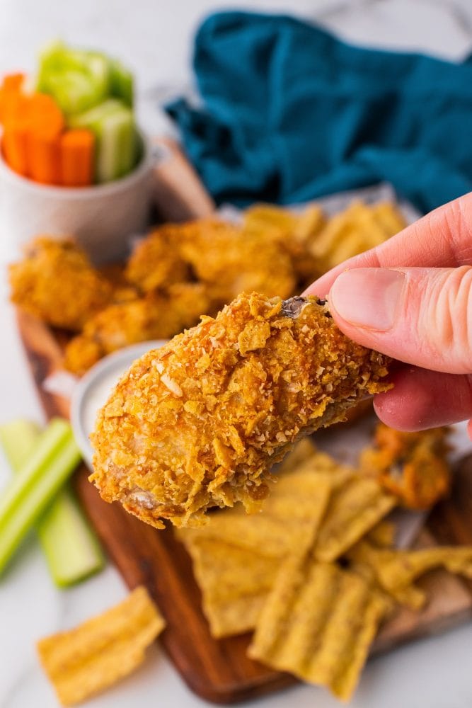 Right hand picking up a single wing showing the crispy texture from the crushed chips.