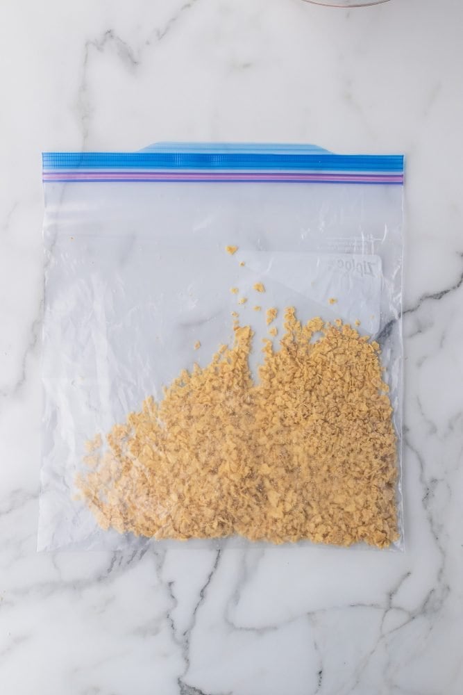Crushed sunchips inside a ziplock bag on top of a marble counter.