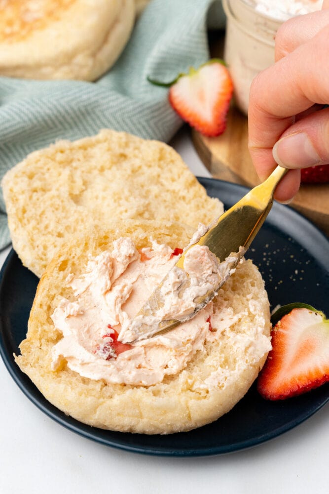 strawberry honey butter being spread onto an English muffin with a gold butter knife.