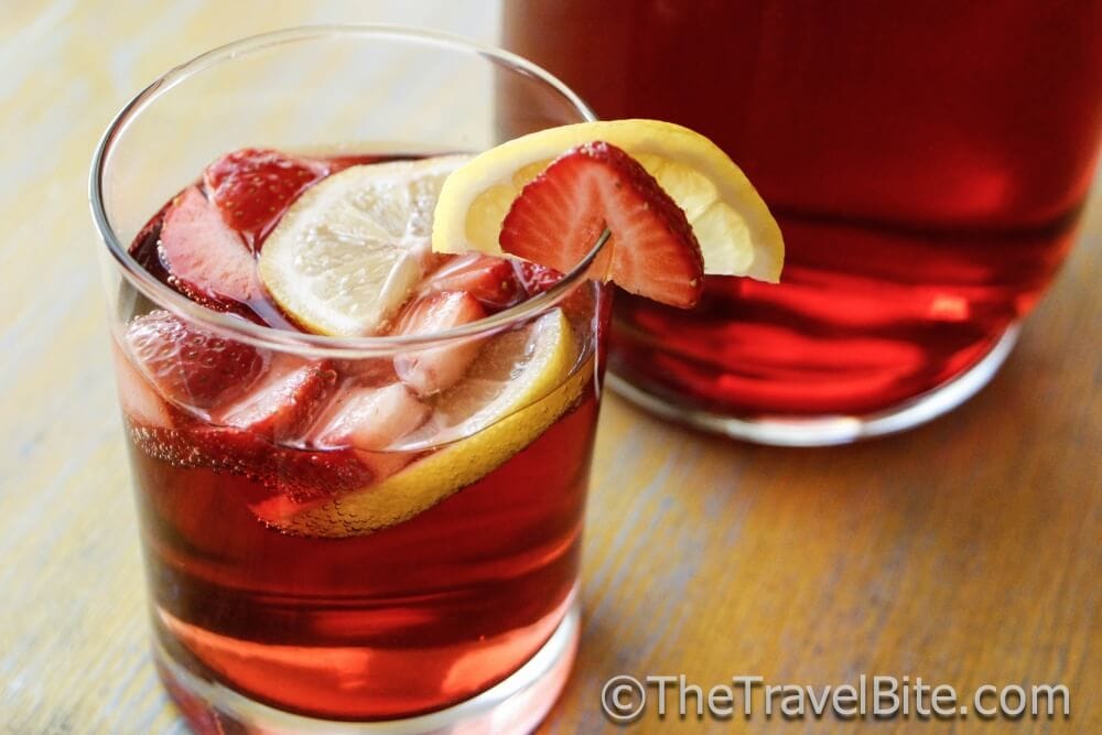 Glass of red sparkling summer sangria with lemon and strawberry slices as garnish.