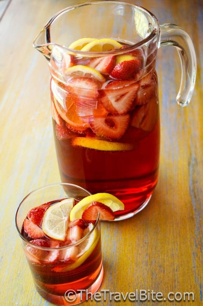 Pitcher of Sparkling Summer Sangria with slices of lemon and strawberry.