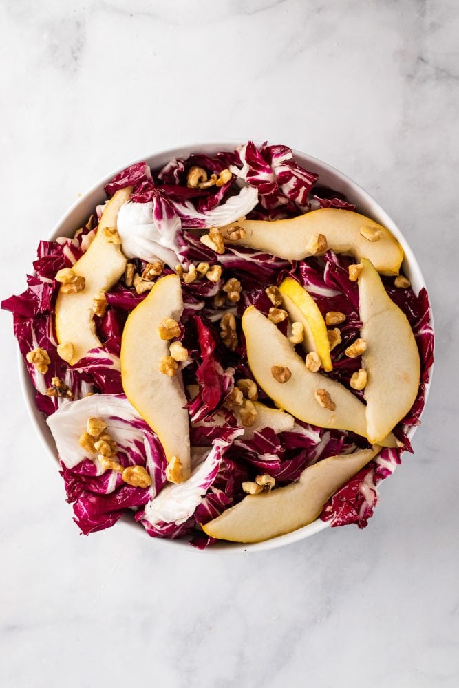 Overhead look at a bowl of radicchio and sliced pears topped with walnuts.