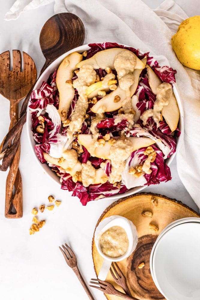 Overhead look at pear salad with walnuts and radicchio in a big bowl with wood salad tongs read to serve.