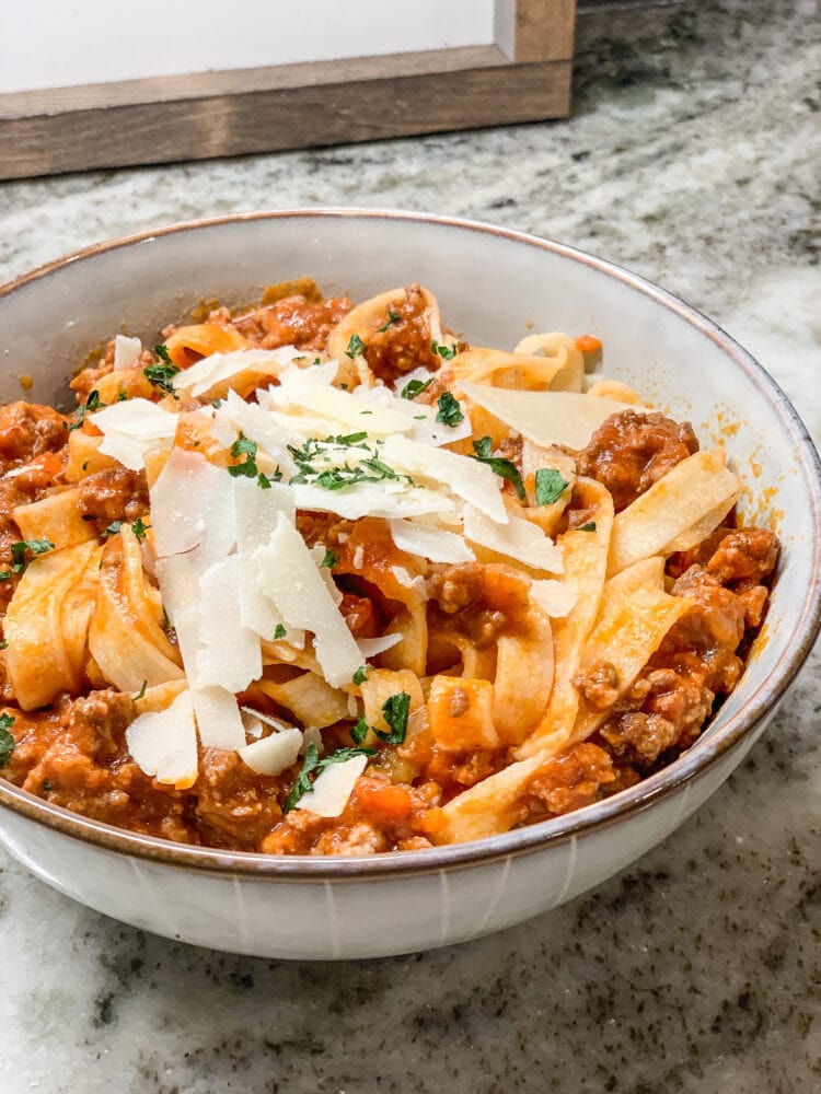 Bowl of fettuccine with Bolognese sauce and topped with shaved Parmesan and parsley.