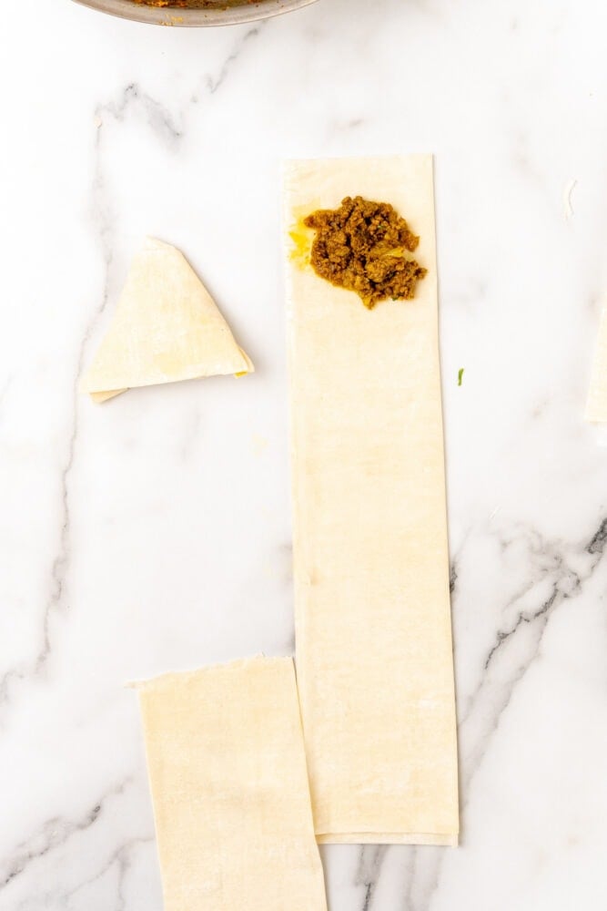raw phyllo dough strip getting folded into a small triangle to create pocket and sealed with samosa filling