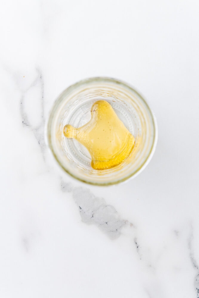 A teaspoon of honey at the bottom of a small mason jar.