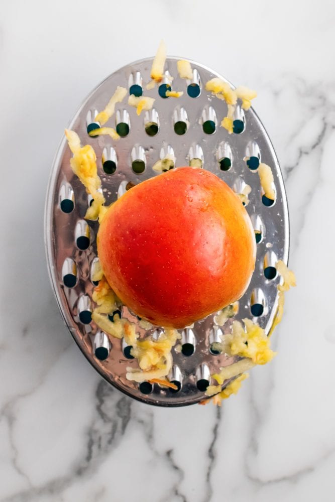 Half an apple in the process of being grated on a metal grater.