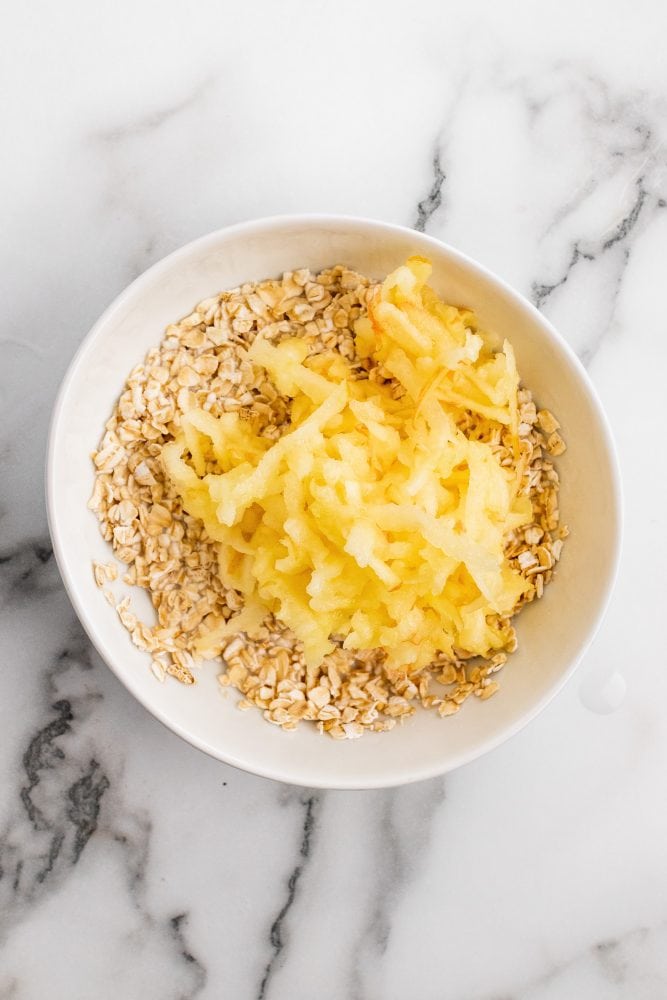 Rolled oats and milk in a white bowl, topped with grated apple.