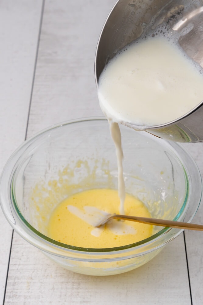 Pouring sauce pan of hot milk into egg yolk and corn starch in a mixing bowl.