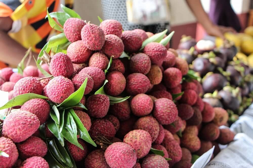 Bright pink lychee fruit stacked in a pyramid at a market in Myanmar.