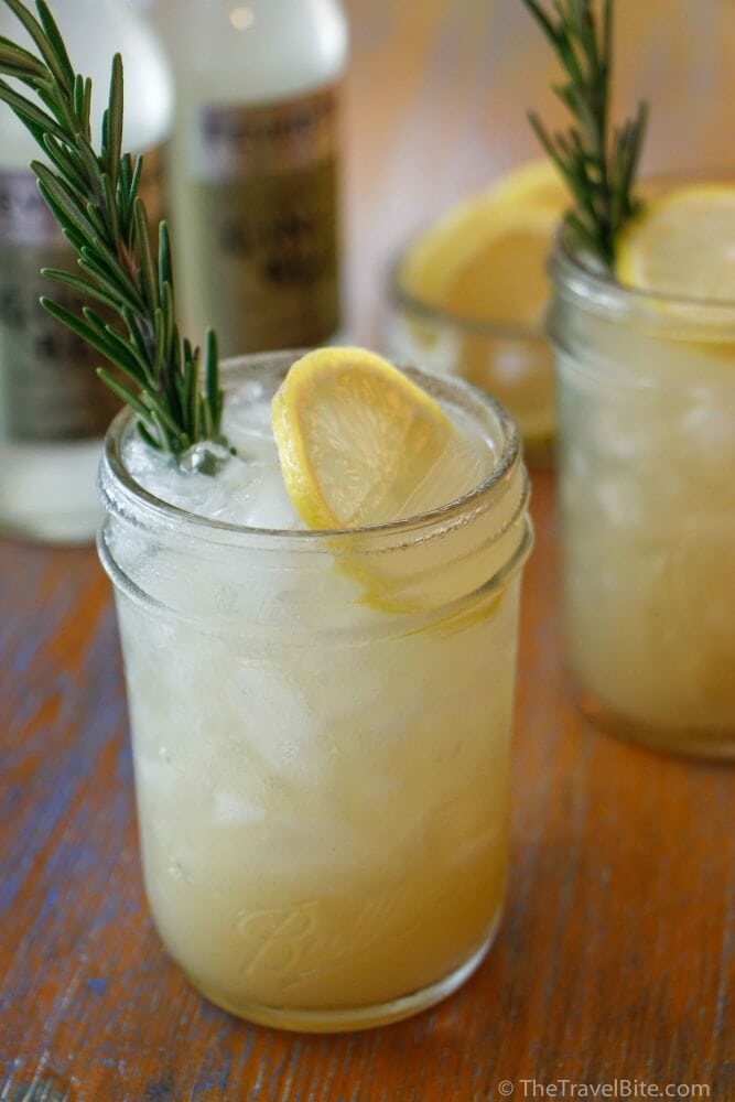 lemon rosemary gin fizz cocktail on wood table with fresh sprig of rosemary and slice of lemon.