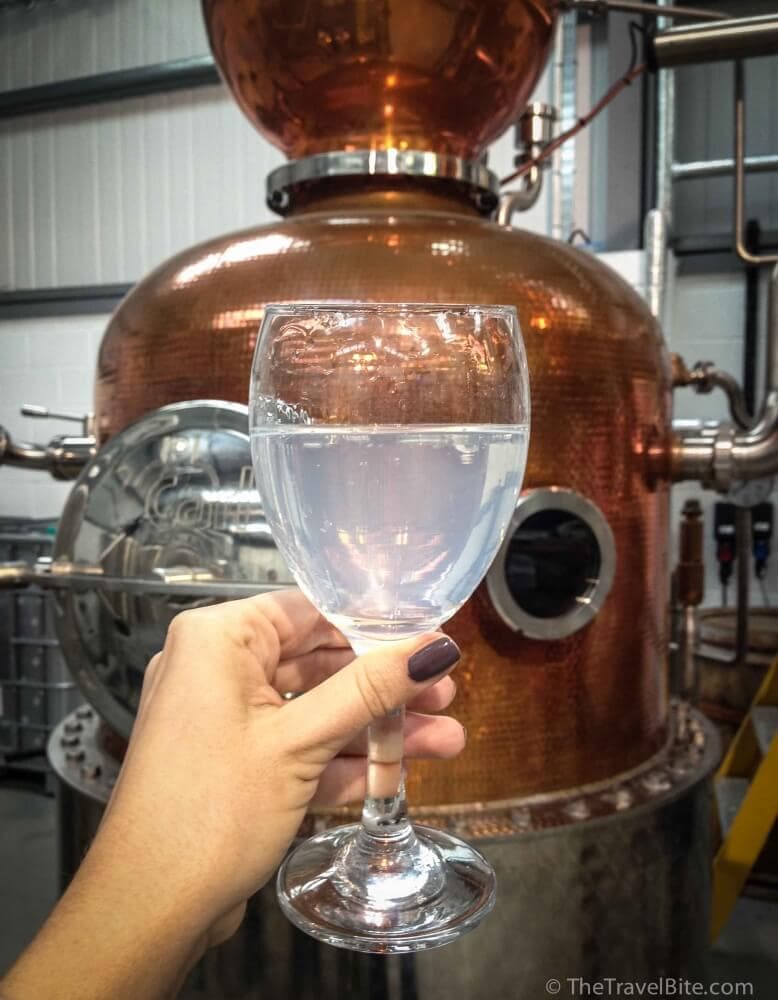 A glass of gin and tonic (without ice) next to a copper pot still.