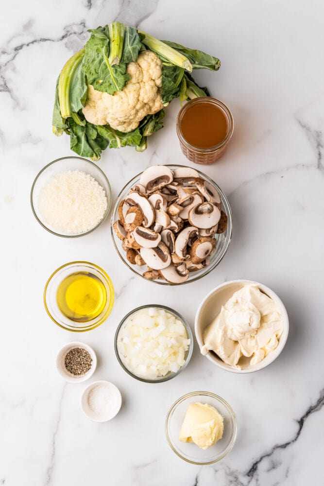 Ingredients for cauliflower risotto including whole cauliflower with leaves, broth, parmesan cheese, sliced mushrooms, olive oil, diced onions, mascarpone cheese, butter, salt, and pepper.