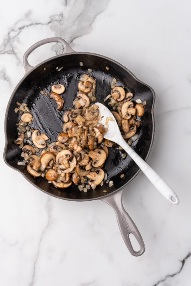 Cooked mushrooms and onions in a grey le creuset skillet