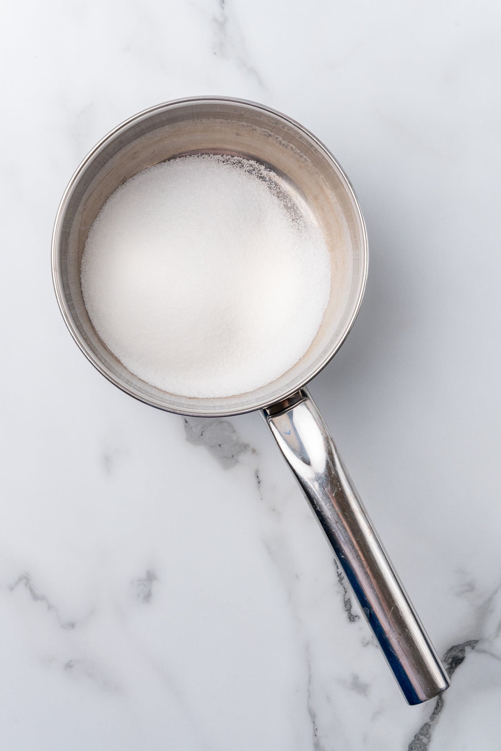 White granulated sugar in a stainless steal sauce pan.