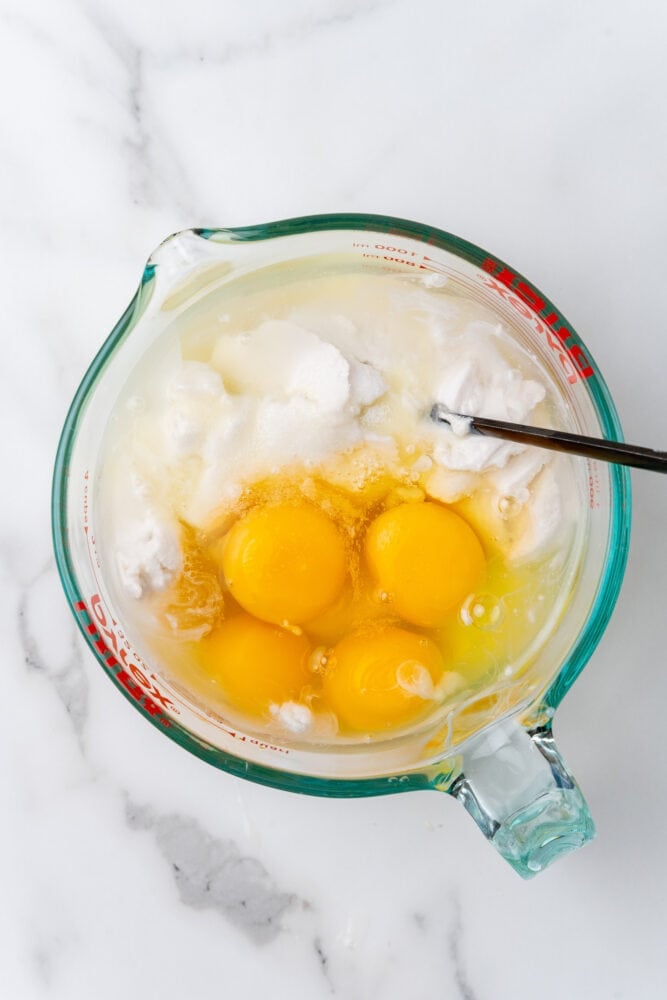 Eggs, sweetened condensed milk, and coconut milk in a glass mixing bowl before blending.